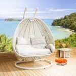 Double seater hanging swing chair in white with soft cushions, placed in a modern outdoor setting.