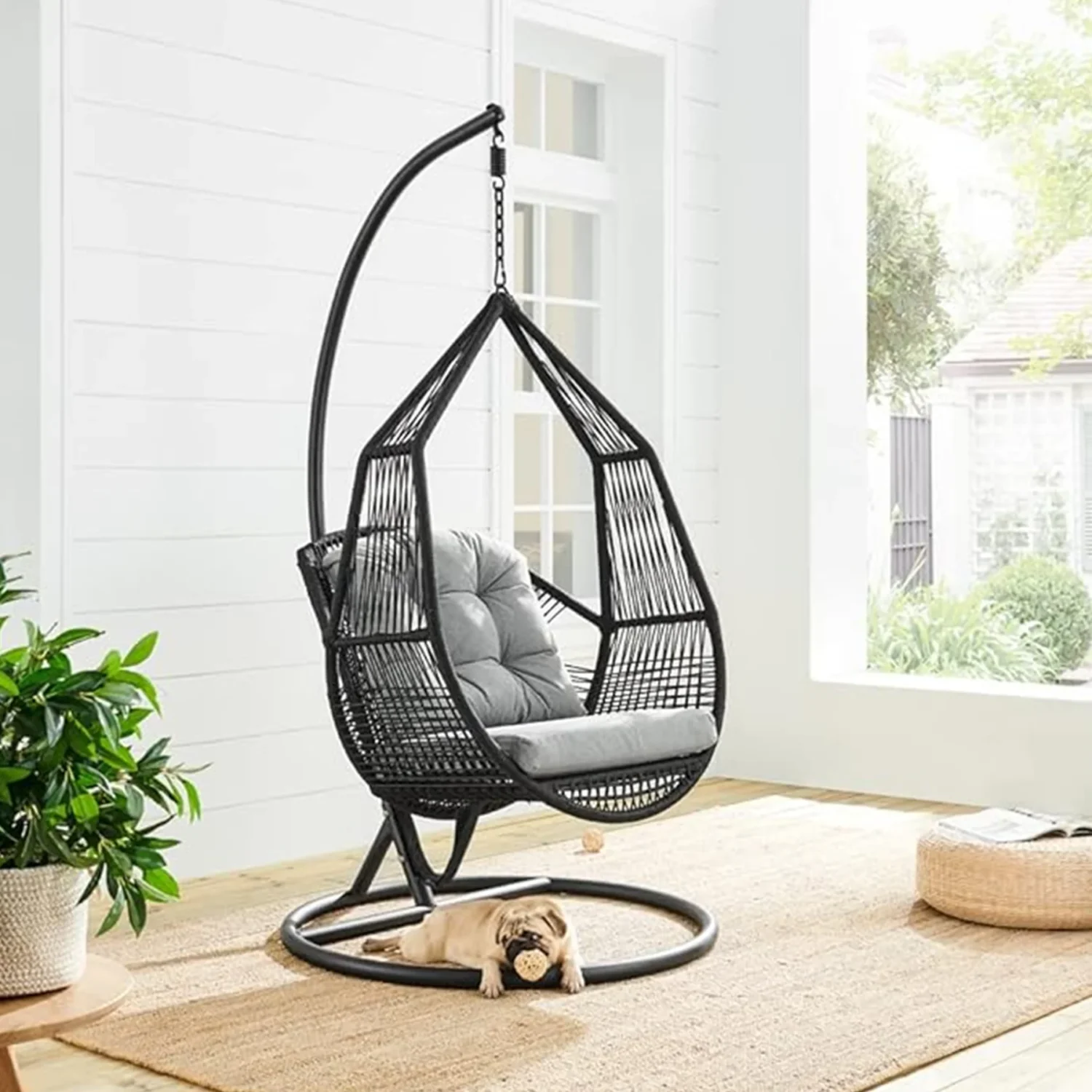 Single-seater hanging swing with a black braided rope and metal stand, placed in a garden setting.