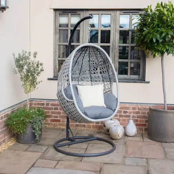 Single seater hanging swing with silver frame and grey cushioned seat placed in a garden.