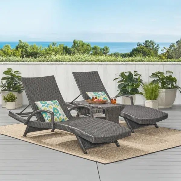 Black outdoor chaise lounge set with matching side table on a patio with greenery in the background.