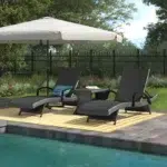 Black outdoor chaise lounge set with matching side table on a patio with greenery in the background.