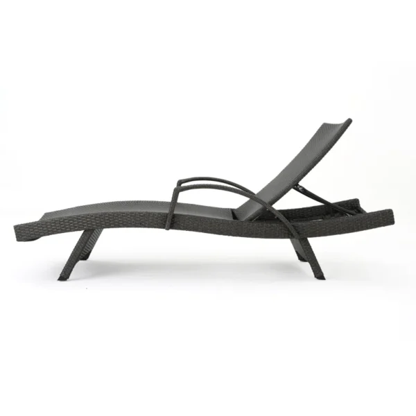 Black outdoor chaise lounge set with matching side table on a patio with greenery in the background.