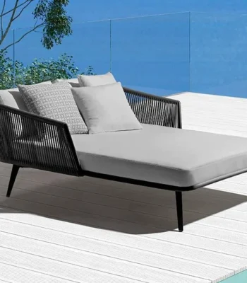 Black and grey patio rope daybed set with cushions placed outdoors on a wooden deck surrounded by greenery.