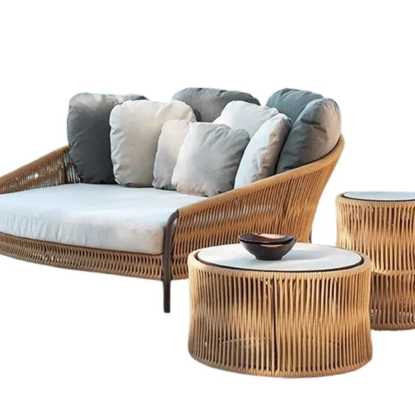 Beige and off-white outdoor rope daybed with plush cushions on a wooden deck surrounded by greenery.