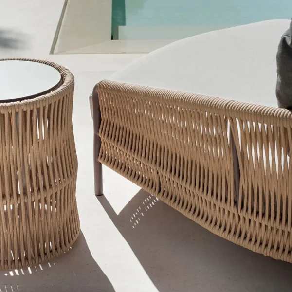 Beige and off-white outdoor rope daybed with plush cushions on a wooden deck surrounded by greenery.