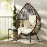 Brown single seater swing basket hanging in balcony with cushions.