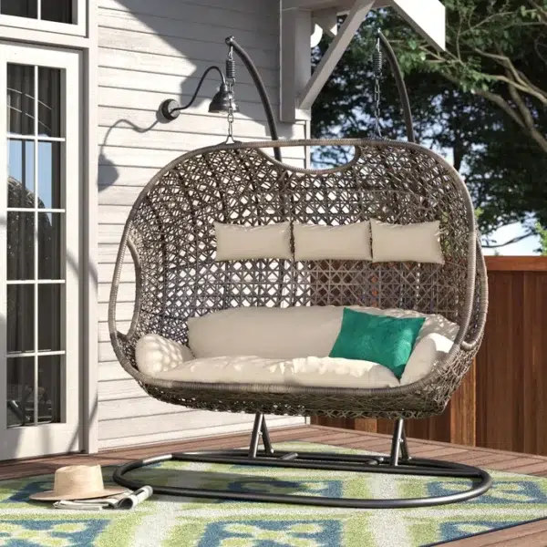 Three-seater hanging swing with sturdy stand in dark brown frame and cream cushions, perfect for balcony or garden relaxation.