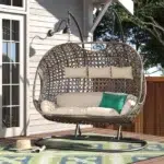 Three-seater hanging swing with sturdy stand in dark brown frame and cream cushions, perfect for balcony or garden relaxation.