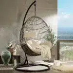 Beige single seater hanging swing with a sturdy stand placed in a garden or balcony setting.