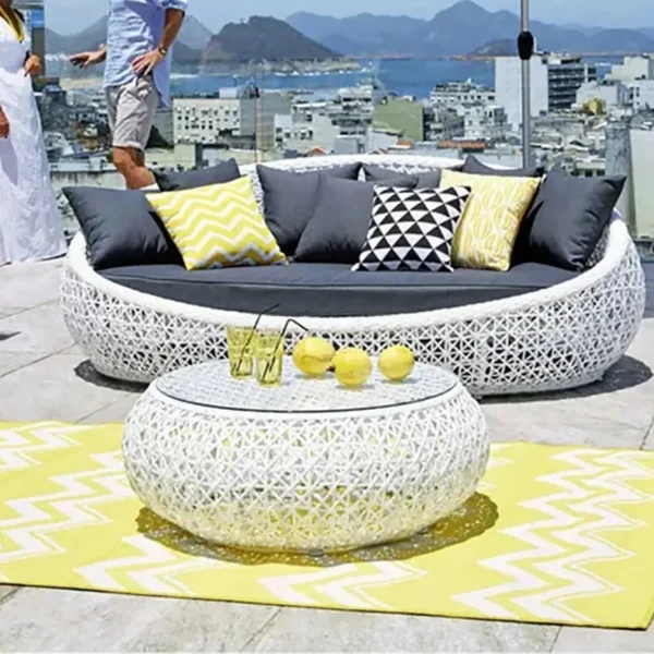 White outdoor rattan wicker daybed set with cushions and matching glass-top table for patio and garden spaces.