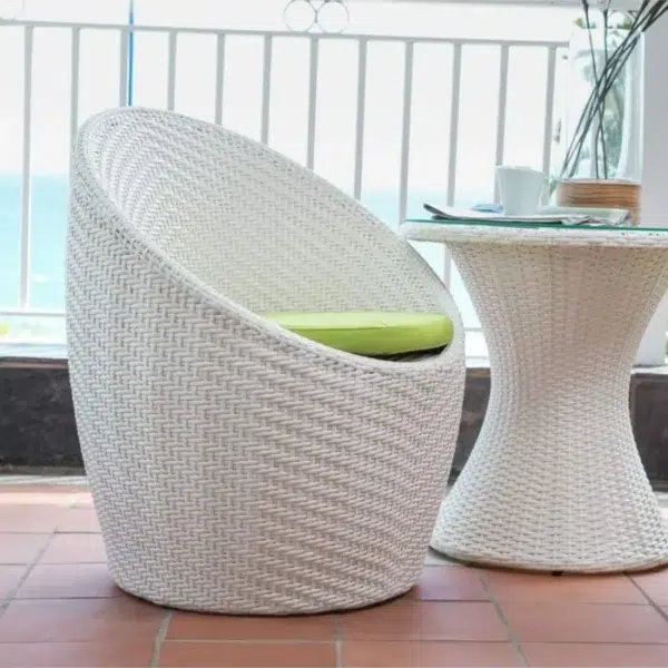 White 3-piece rattan wicker patio set with two chairs and a glass-top table on a balcony overlooking the sea.