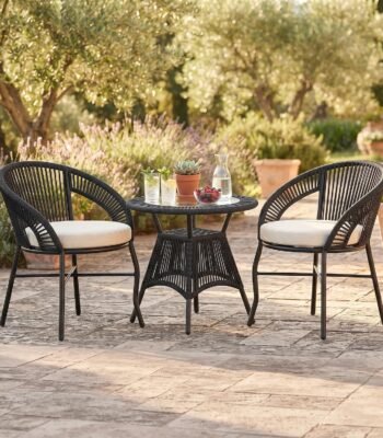 3-piece outdoor rope patio furniture set with two black handwoven rope chairs, cream cushions, and a round matching table in a garden patio setting.