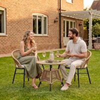 2 Seater Outdoor Patio Furniture Set with Two Rope Woven Chairs, Cream Cushions and Round Glass Top Table, with a Couple Relaxing in a Garden Setting