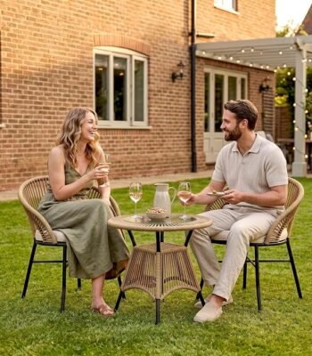 2 Seater Outdoor Patio Furniture Set with Two Rope Woven Chairs, Cream Cushions and Round Glass Top Table, with a Couple Relaxing in a Garden Setting